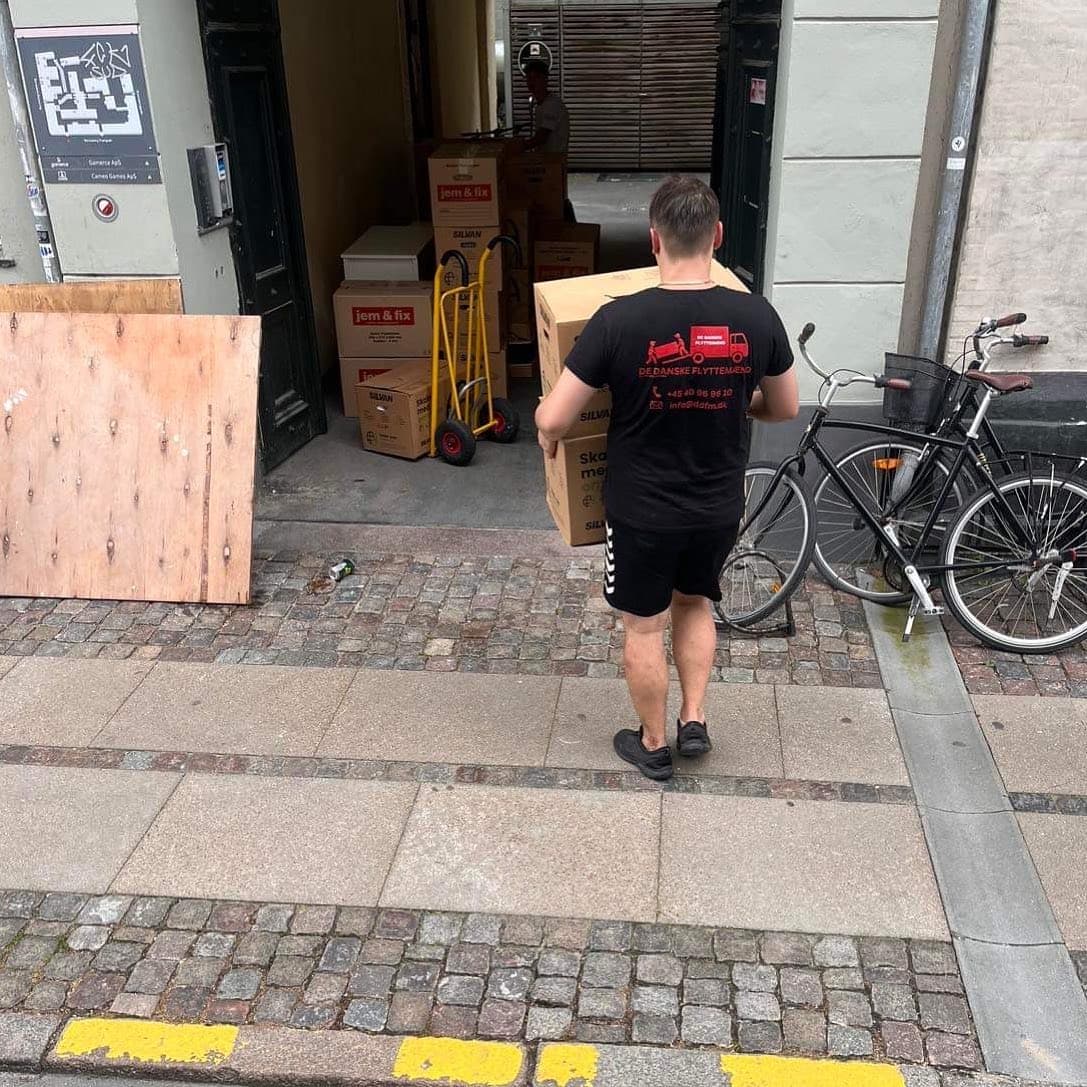 Flyttemand bærer papkasser hen over fortovet mod en opgang